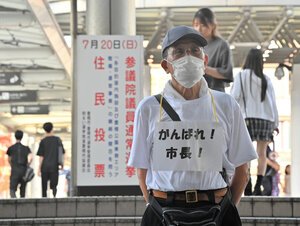 豊橋駅東口に立つ男性。首から｢がんばれ！　市長！｣のカードをぶら下げていた=2025年7月13日、愛知県豊橋市花田町、戸村登撮影
