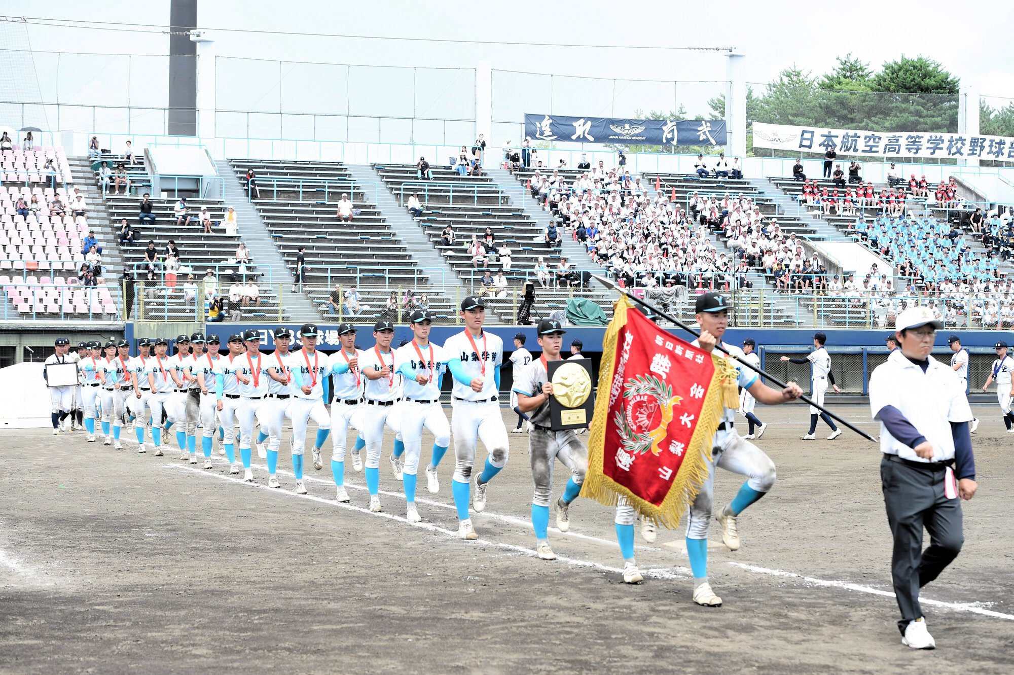 閉会式が終わり、優勝旗を持って行進する山梨学院の選手たち=2025年7月23日、山日YBS