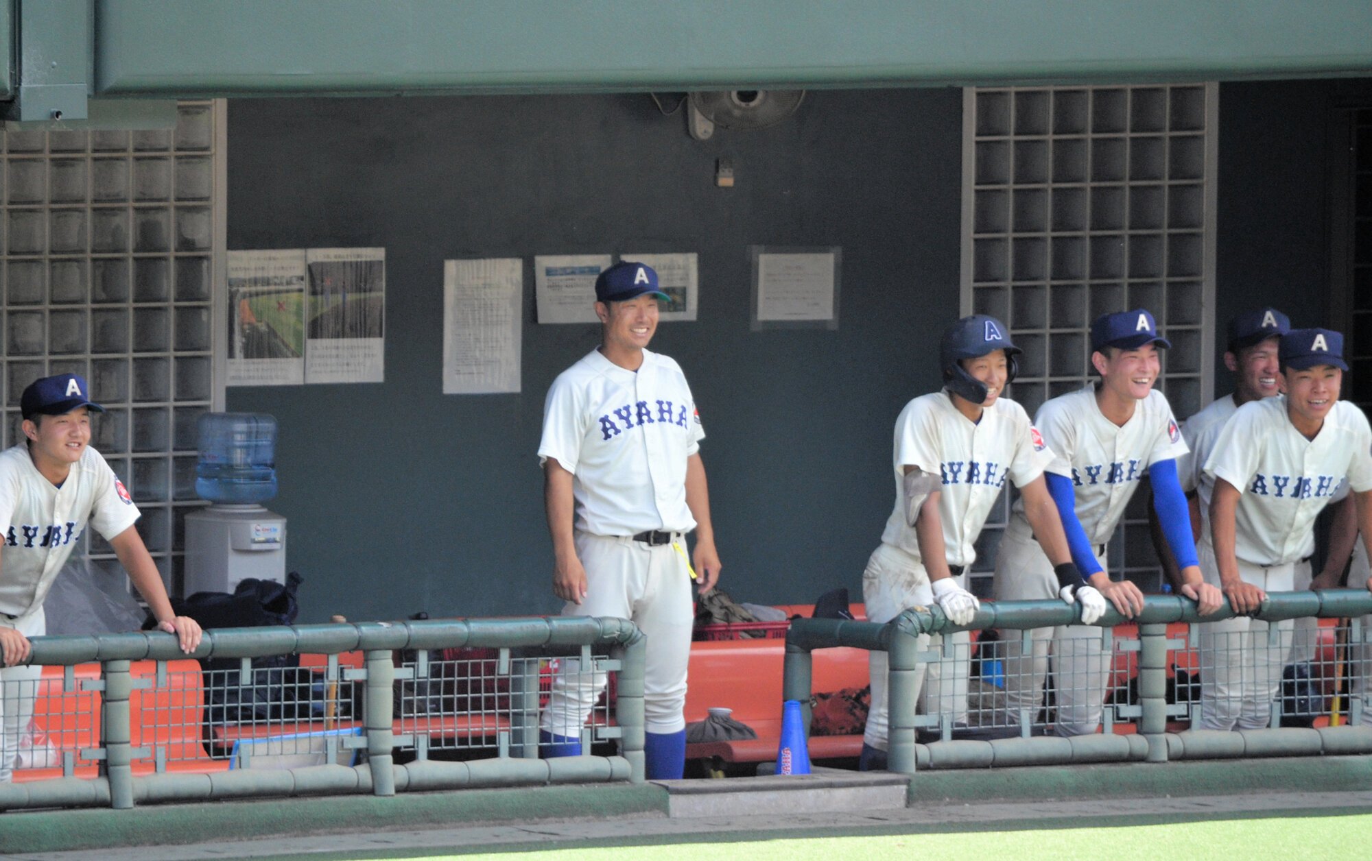 滋賀学園と戦った滋賀大会決勝の綾羽のベンチ。千代純平監督が中央に立って白い歯を見せ、笑顔の選手もいる=2025年7月26日午前11時21分、皇子山、仲程雄平撮影