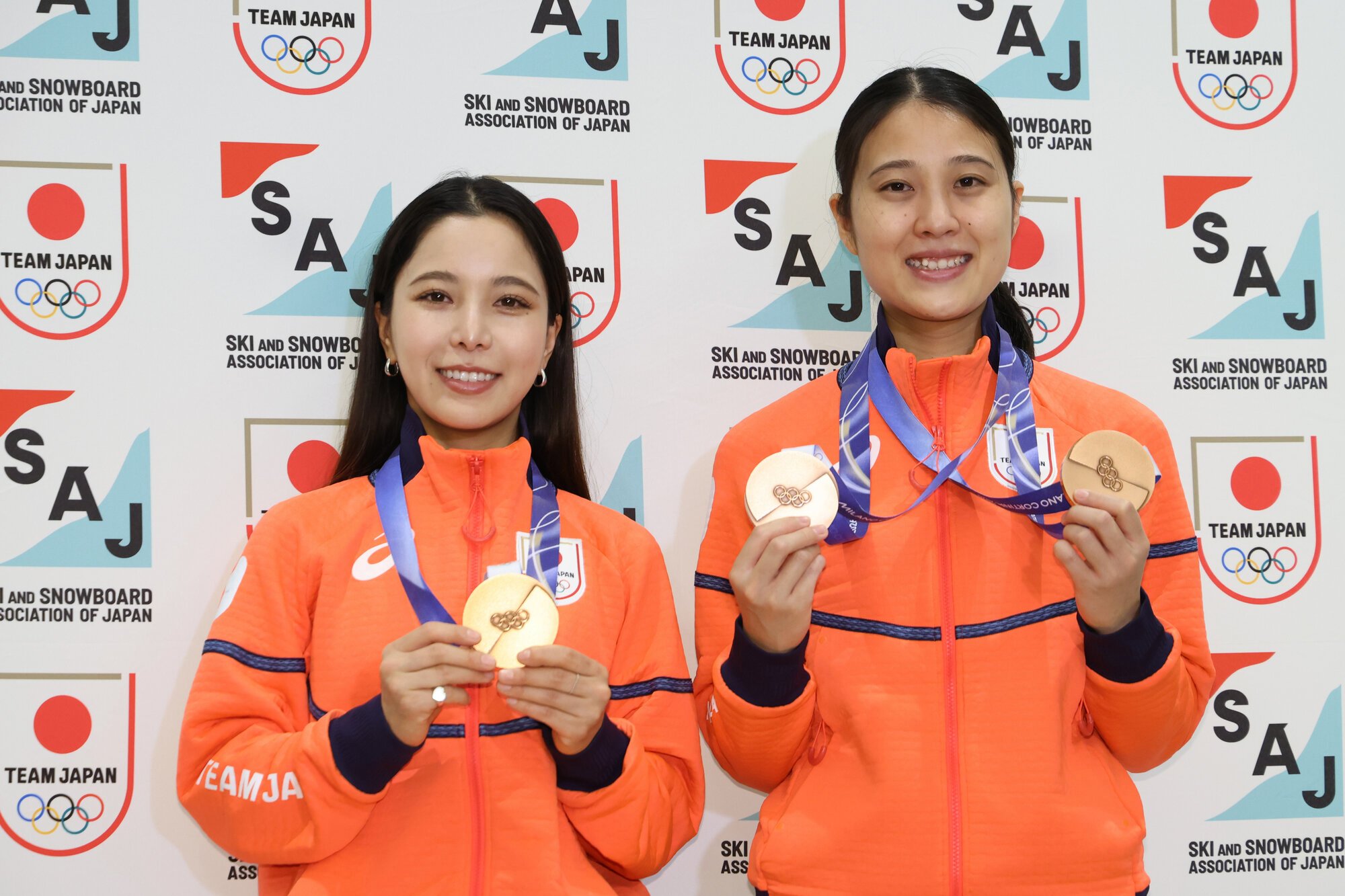 帰国後の記者会見で写真撮影に応じる、ノルディックスキー･ジャンプ女子の丸山希(右)と高梨沙羅=2026年2月18日午前9時3分、羽田空港、友永翔大撮影