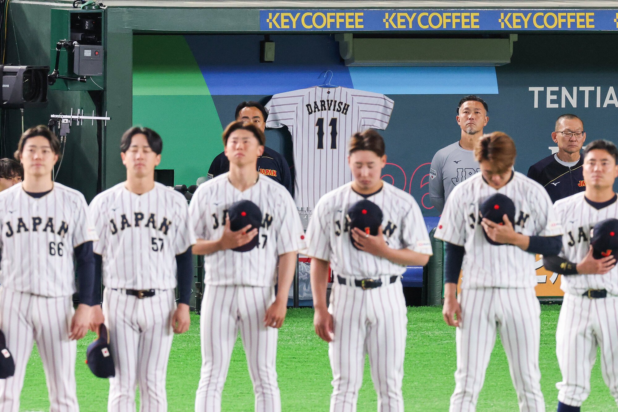 国歌斉唱する日本の選手たち。ベンチにはダルビッシュ有のユニホームが掲げられている=友永翔大撮影