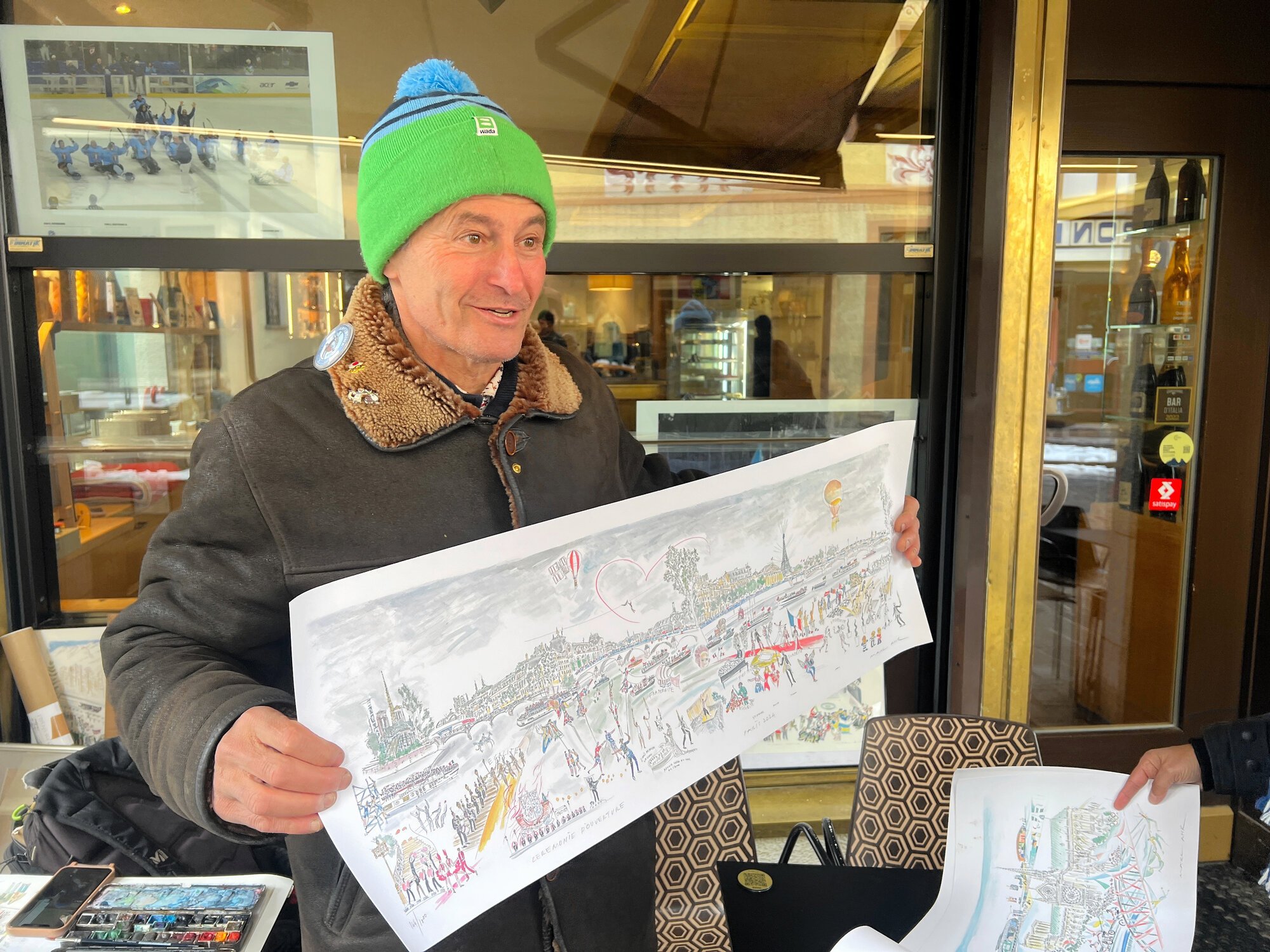 コルティナダンペッツォの街中で描いた水彩画を持つマーク･アーさん=2026年3月15日午後3時1分、コルティナダンペッツォ、比嘉展玖撮影