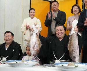 千秋楽パーティー会場で、左から師匠の音羽山親方、長女アヤゴーちゃん、後援会関係者らの祝福を受けながらお祝いのタイを持ち上げる霧島。後方左は音羽山夫人＝2026年3月22日