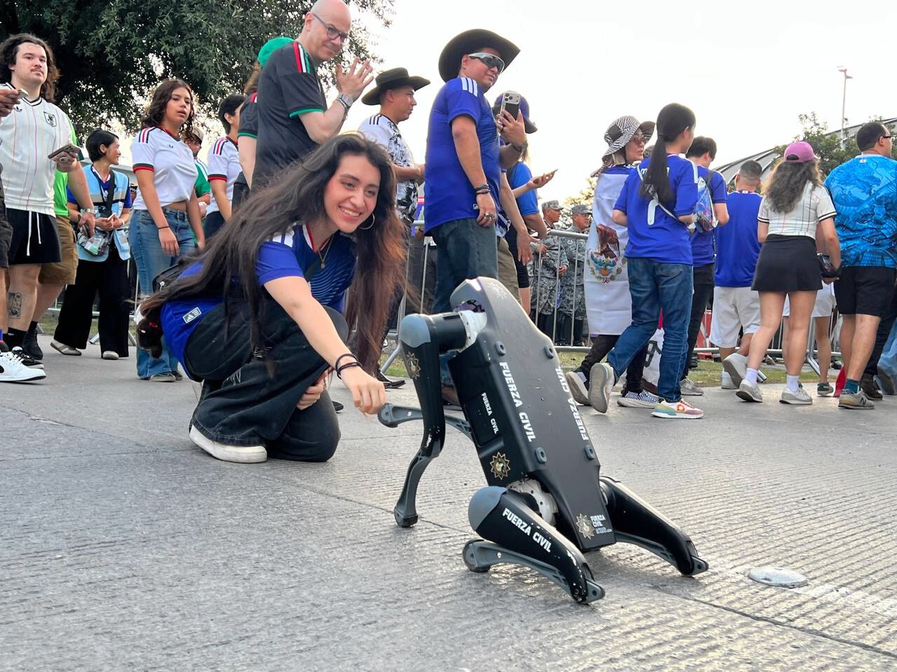 メキシコ･モンテレイのスタジアム周辺で2026年6月20日(現地時間)、警戒中の犬型ロボットとグータッチする観客=河崎優子撮影