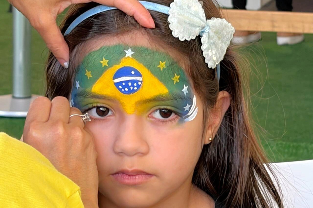 公園内のパブリックビューイングのための特設スペースで、ブラジル国旗をあしらった模様のフェースペイントをしてもらう子ども=2026年6月27日、サンパウロ、河崎優子撮影