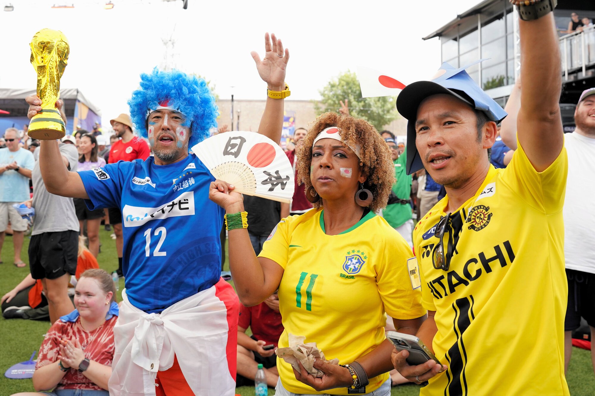 米ヒューストンで開かれているサッカーワールドカップの公式イベントでエールを送る、カリフォルニア州在住の長岡宏一さん(左)と妻でブラジル出身のイレイニさん(中央)。イレイニさんは日本とブラジルの激突に｢複雑だけど2―1で日本が勝つことを願っている｣という=2026年6月28日、田中恭太撮影