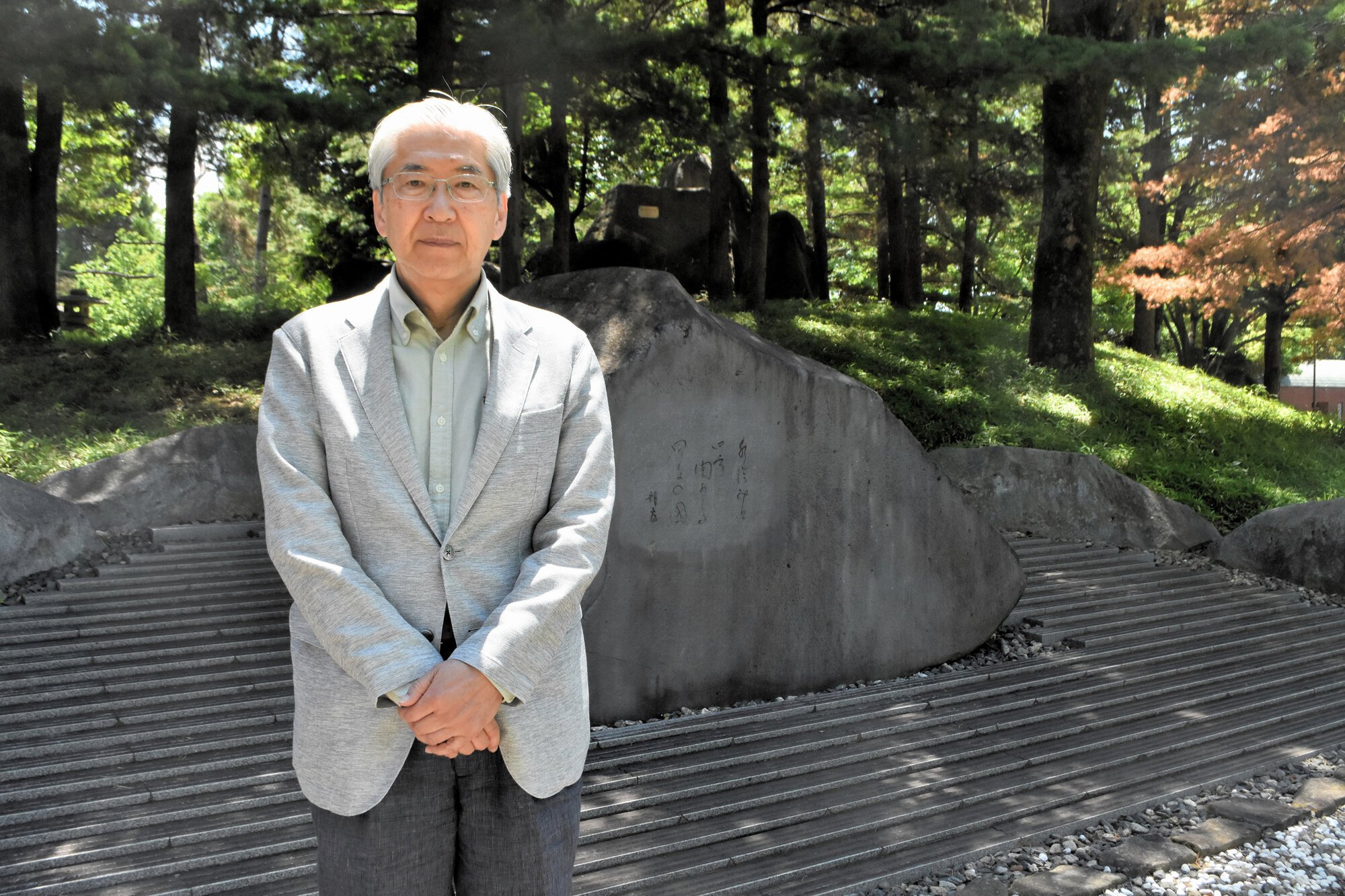 飯田蛇笏の四男で俳人の龍太(1920～2007)に師事した俳人･井上康明さん。後ろの碑は、龍太の代表句の一つ、｢水澄みて四方(よも)に関ある甲斐の國(くに)｣の句碑=2026年5月14日、甲府市貢川1丁目、二階堂勇撮影