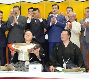 千秋楽パーティーで関係者の祝福を受けながら銀杯にそそがれたお酒を飲む大の里。右は師匠の二所ノ関親方(撮影･小沢裕)
