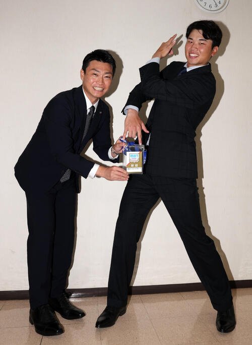 指名あいさつを受けた東京ガスの藤沢涼介(右)は、ジョジョ立ちして、ヤクルト青木宣親GMからドラフト会議IDを受け取る(撮影･浅見桂子)